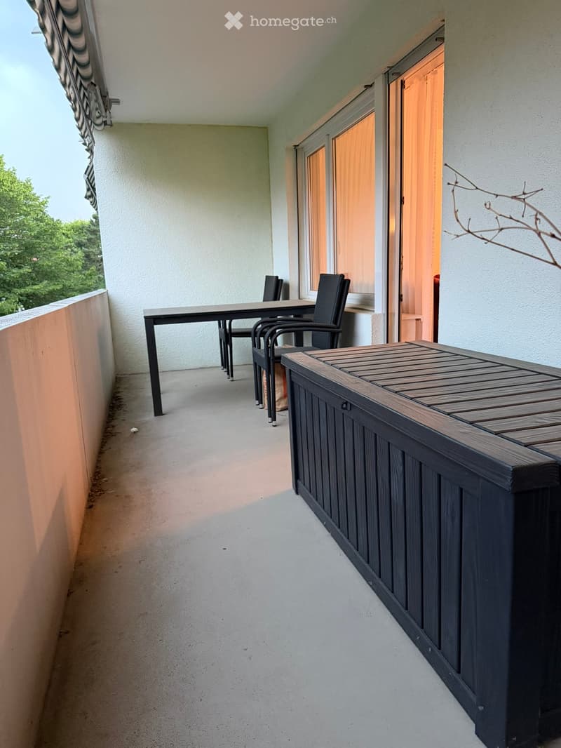Balcony with a table and chairs, wooden planter box, and open door leading inside.