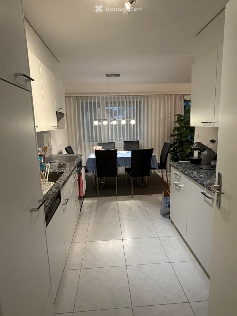 Open-plan kitchen and dining area with white cabinets, granite countertops, and a dining table with chairs.