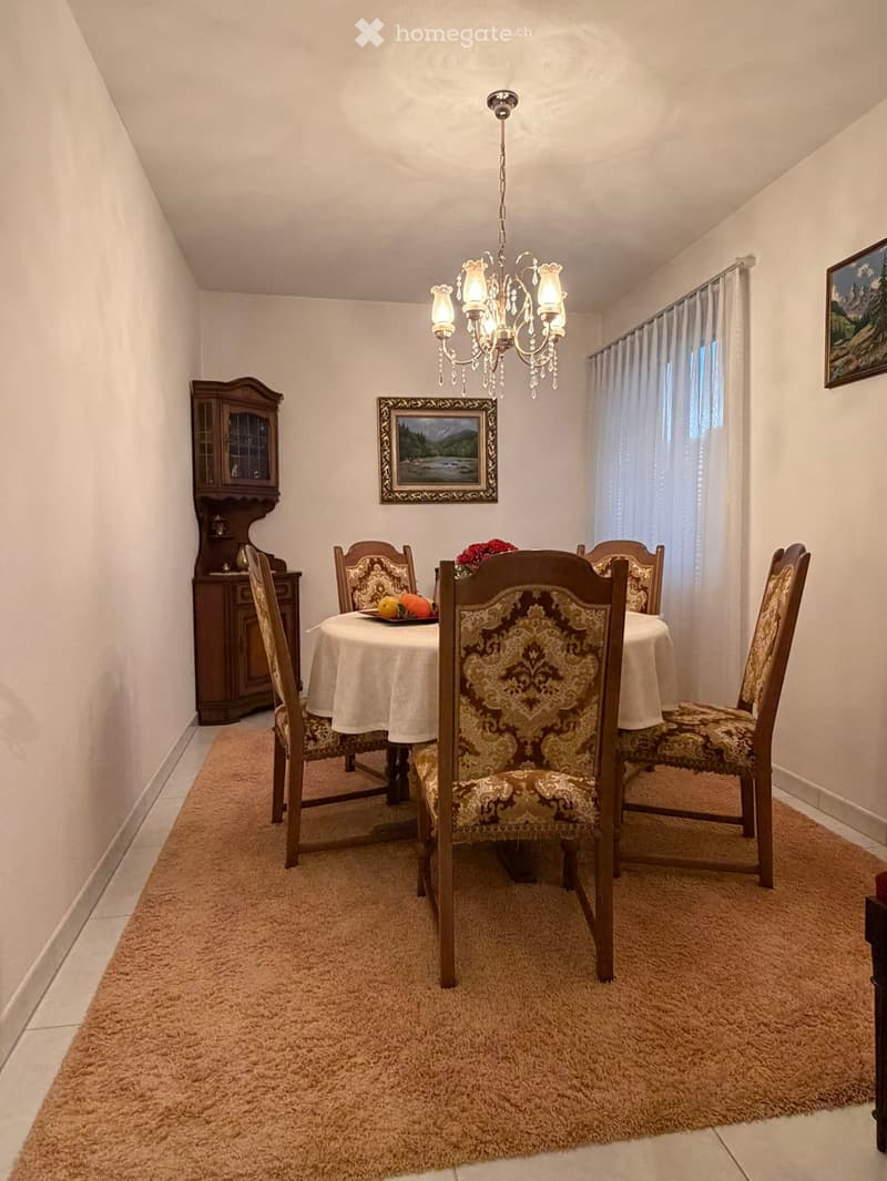 Dining room with a round table, six chairs, chandelier, cabinet, and artwork on the walls.