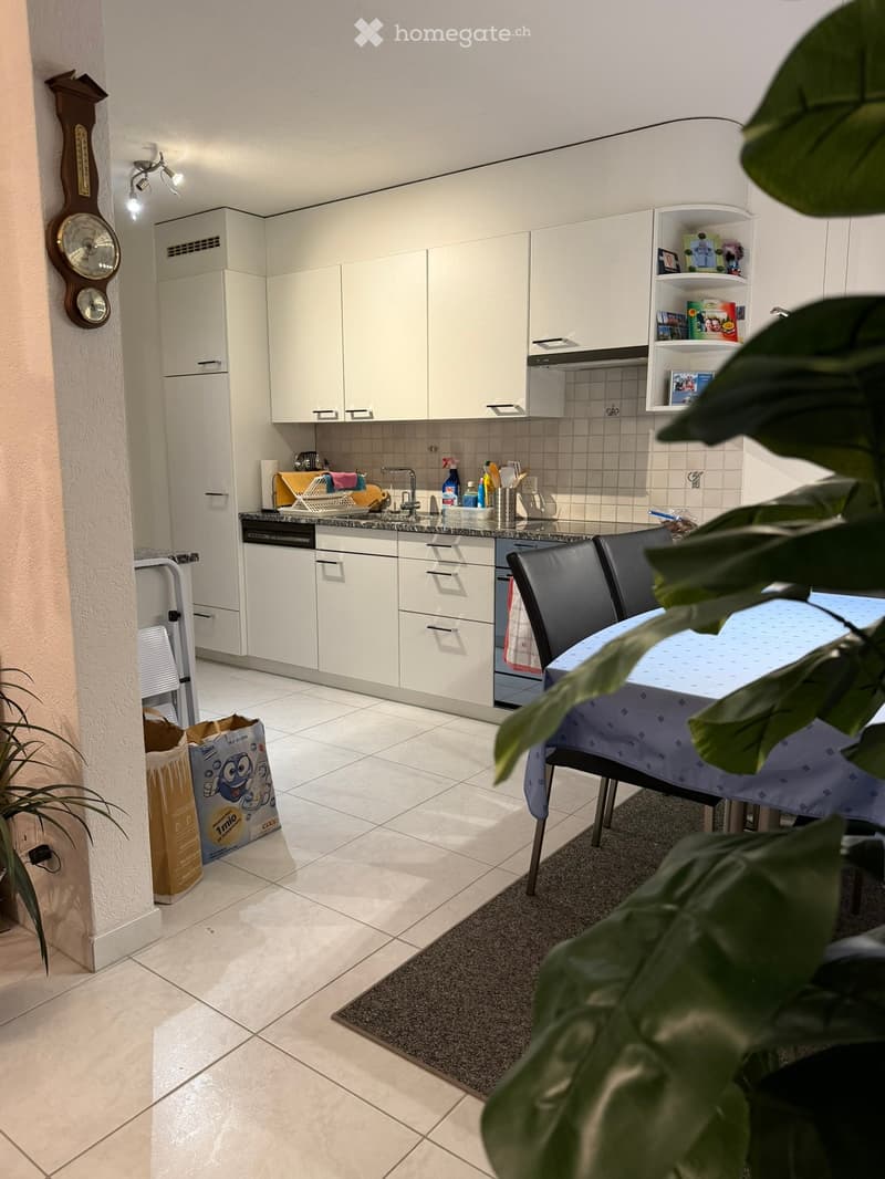 Modern kitchen with white cabinets, granite countertop, dishwasher, and a small dining area with a table and chairs.