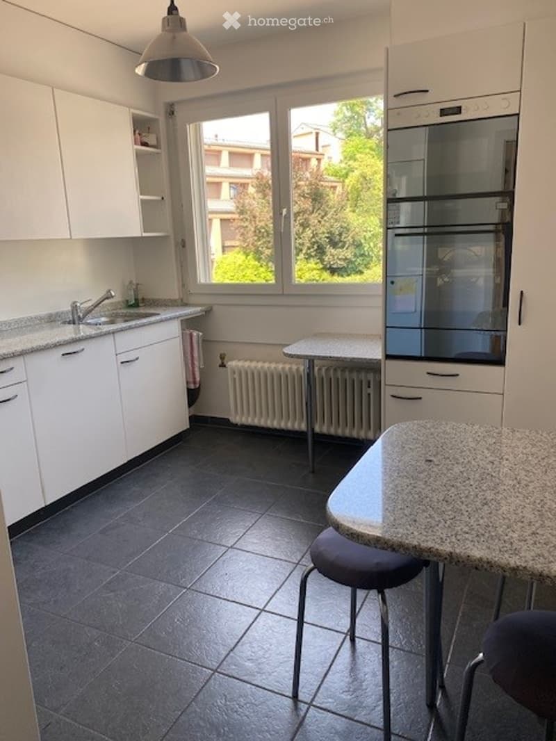 Modern kitchen with white cabinets, granite countertops, stainless steel appliances, and a small dining area with a table and stools.