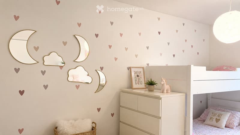 A cozy children's bedroom with a bunk bed, a dresser, decorative mirrors, a picture frame, a small plant, and a basket with a fluffy pillow.