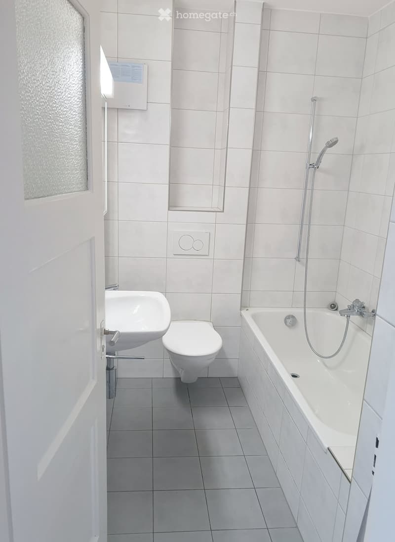 Modern bathroom with white tiles, bathtub, toilet, and sink.