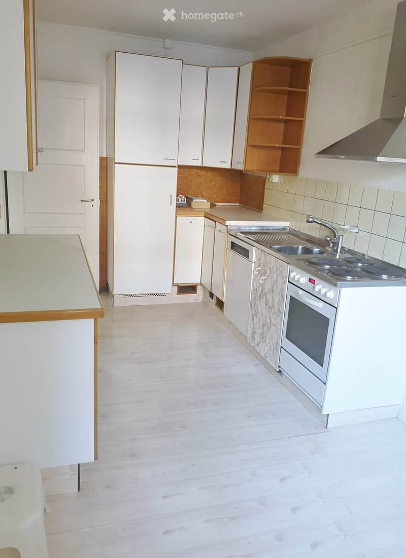 Modern kitchen with white cabinets, a refrigerator, an oven, a sink, and a faucet. The floor is light wood, and the walls are tiled.