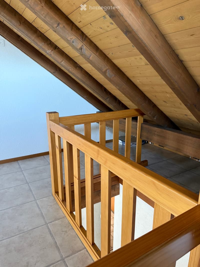 Wooden staircase with a slanted wooden ceiling and tiled floor, leading to an attic space.