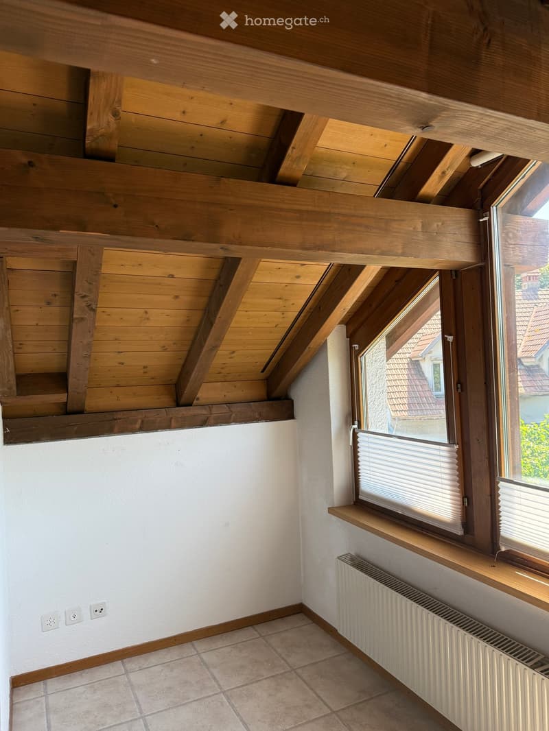 Empty attic room with wooden slanted ceilings, tiled floor, radiator, and windows with blinds.