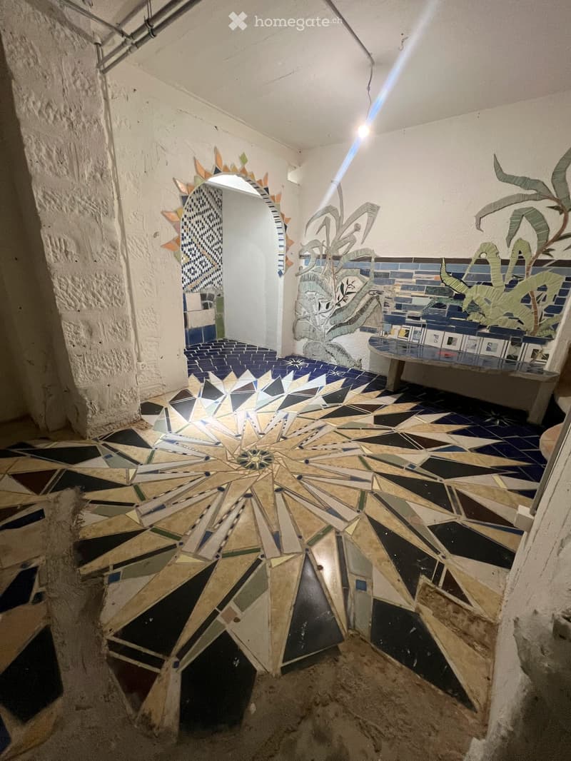 Corridor with geometric mosaic floor, arched doorway, and decorative wall art featuring plants and abstract shapes.