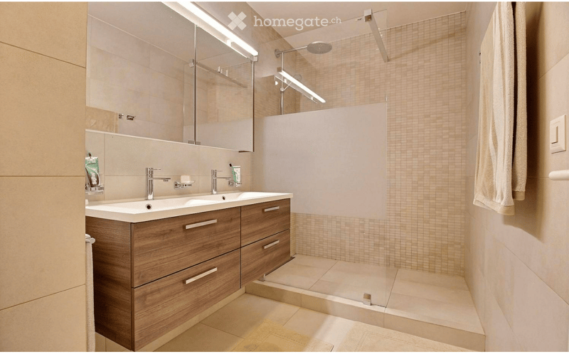 Modern bathroom with a double sink, wooden cabinet, large mirror, and a walk-in shower with a glass enclosure.