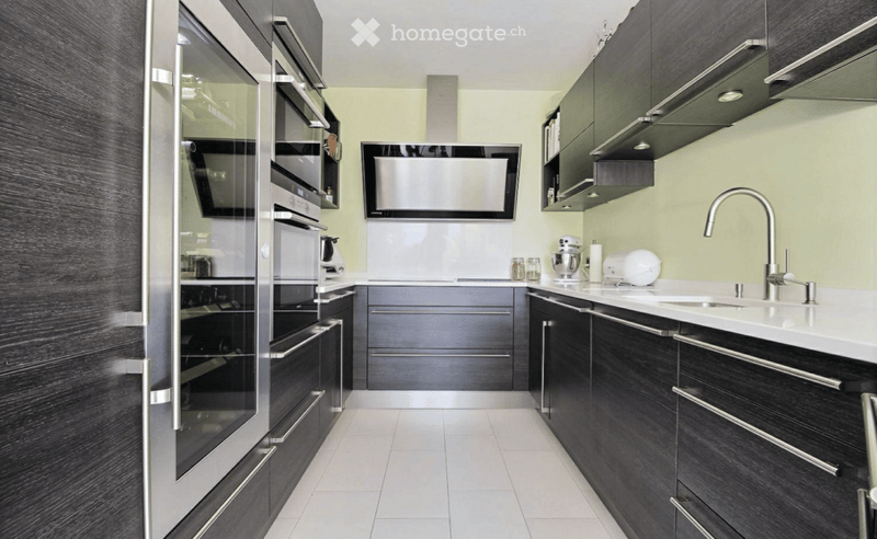 Modern kitchen with dark cabinets, white countertops, stainless steel appliances, and a sleek design.