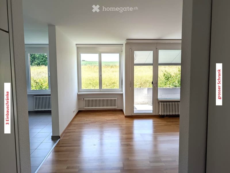 Empty room with wooden flooring, large windows, radiators, and a sliding glass door leading to a balcony.