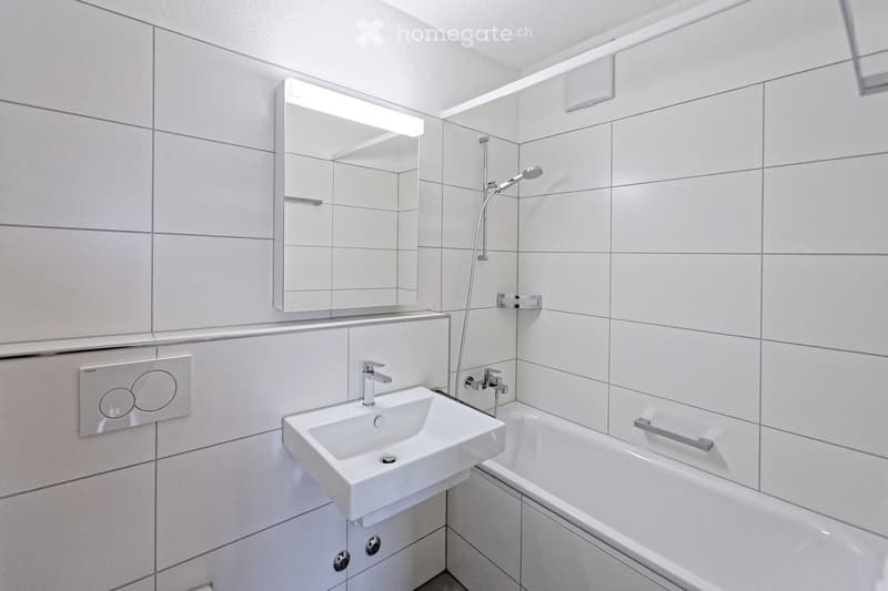 Modern bathroom with white tiles, a sink, bathtub, mirror, and showerhead.