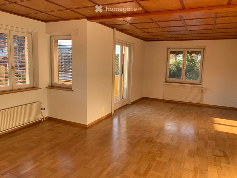 Empty room with wooden flooring, white walls, multiple windows, radiators, and a sliding glass door leading outside.