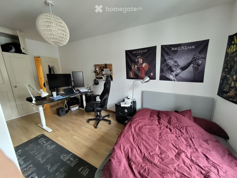 A furnished bedroom with a bed, desk, chair, laptop, and posters on the wall.