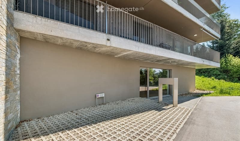 Modern building with a raised ground floor, featuring a balcony and a glass entrance door.