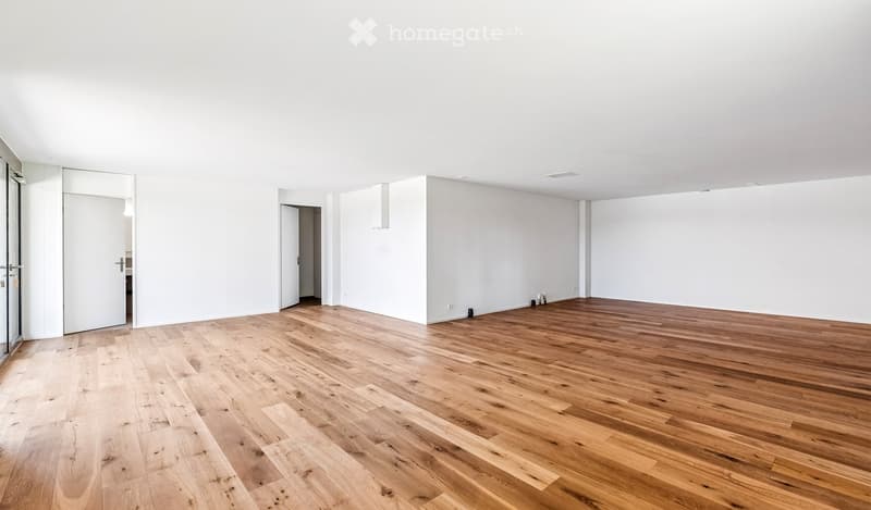 Empty room with light wooden flooring and white walls, featuring a large glass door and several doorways leading to other spaces.