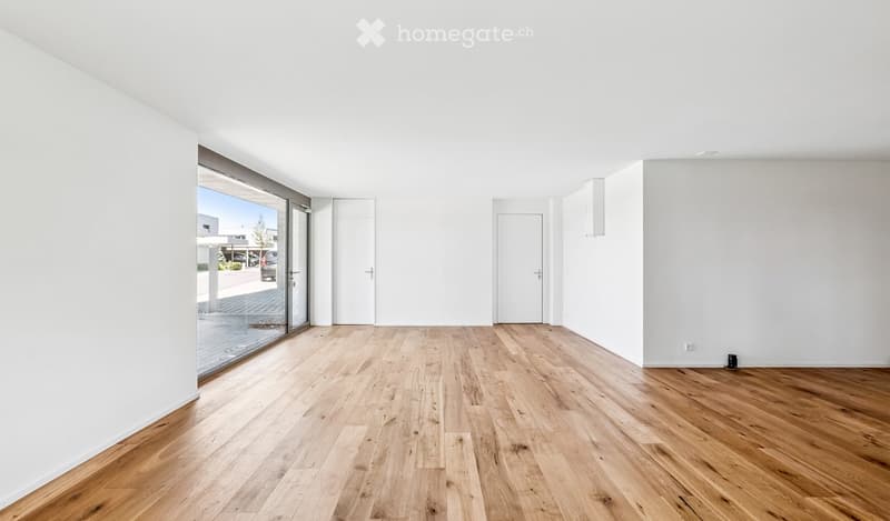 Empty room with light wooden flooring, white walls, and large glass sliding doors leading to an outdoor area.