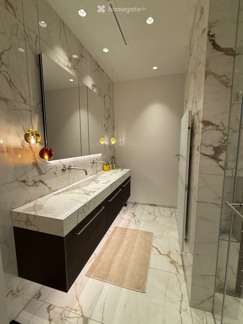 Modern bathroom with marble countertops, a large sink, dark wooden cabinet, and a glass shower enclosure.