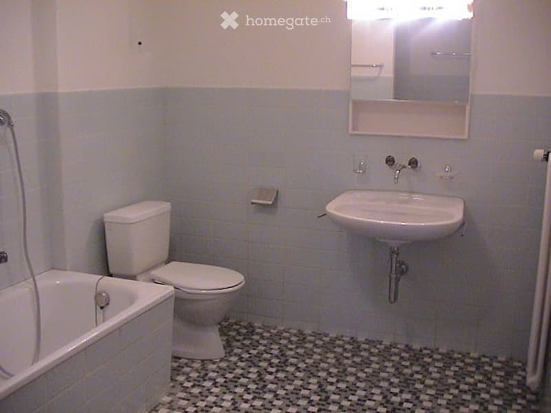 A small bathroom with a white toilet, a white sink, a bathtub, a mirror, and a tiled floor.