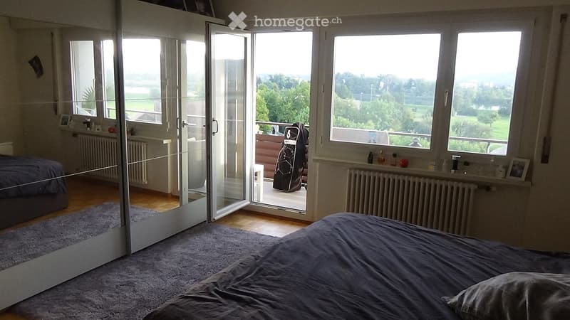Bright bedroom with large windows and a sliding glass door leading to a balcony, featuring a bed, a large mirror, and a radiator.
