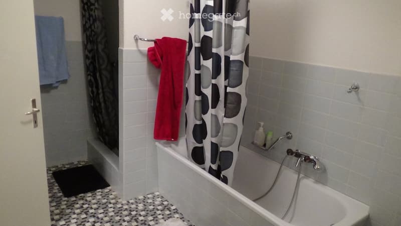 Bathroom with a white bathtub, tiled walls, a shower curtain, and towels hanging on a rack.