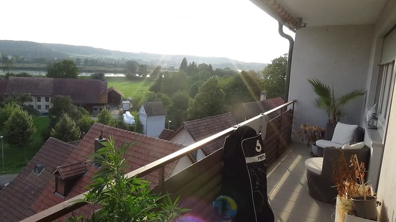 Balcony with a view of a rural landscape, featuring a wicker chair, small table, and potted plants.
