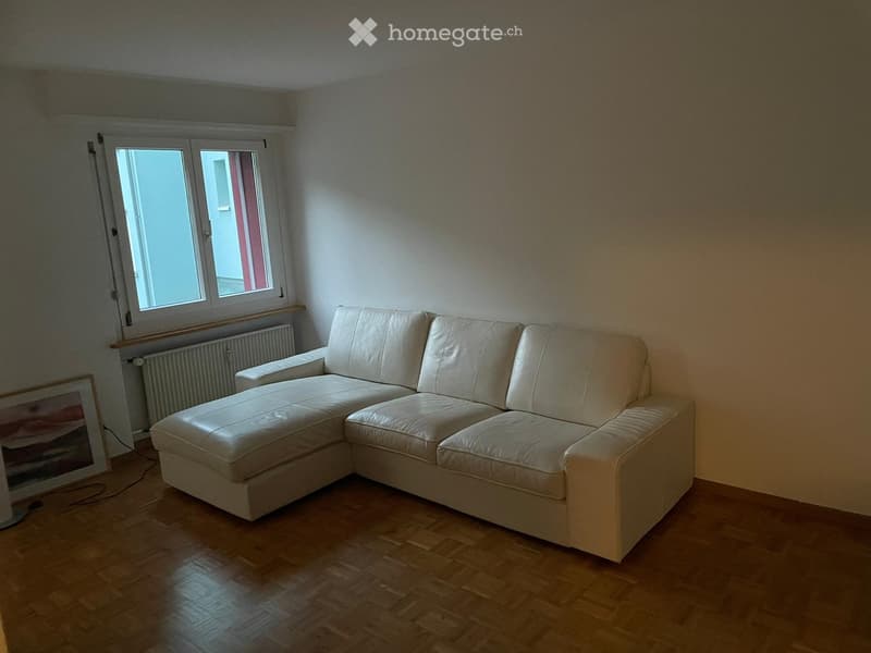 Living room with a white leather sectional sofa, wooden flooring, and a picture frame on the floor near the window.