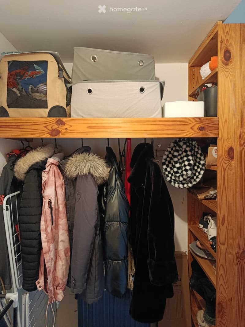 A well-organized closet with wooden shelves, hanging clothes, storage boxes, and a hat on the shelf.