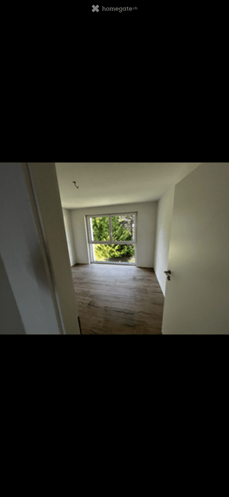 Empty room with wooden flooring and large window letting in natural light. Bare walls and no furniture.
