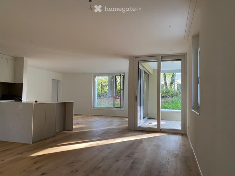 Bright, open-plan room with wooden flooring, large windows, and sliding glass doors leading to an outdoor area.