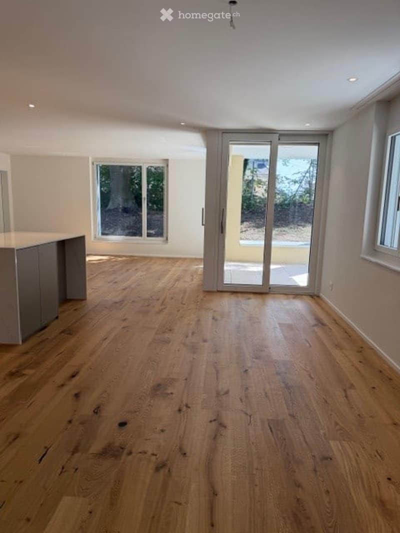Completely empty room with wooden flooring, large windows, and sliding glass doors leading to an outdoor area.