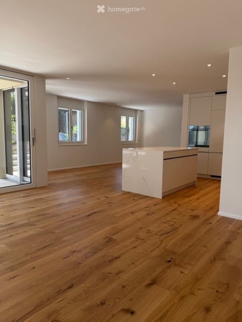 Open-plan space with wooden flooring, large windows, and a central island with built-in cabinets. No furniture or equipment present.