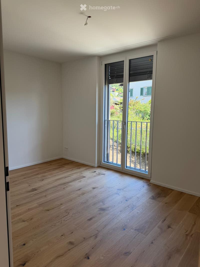 Empty room with wooden flooring, white walls, and large sliding glass doors leading to a balcony.