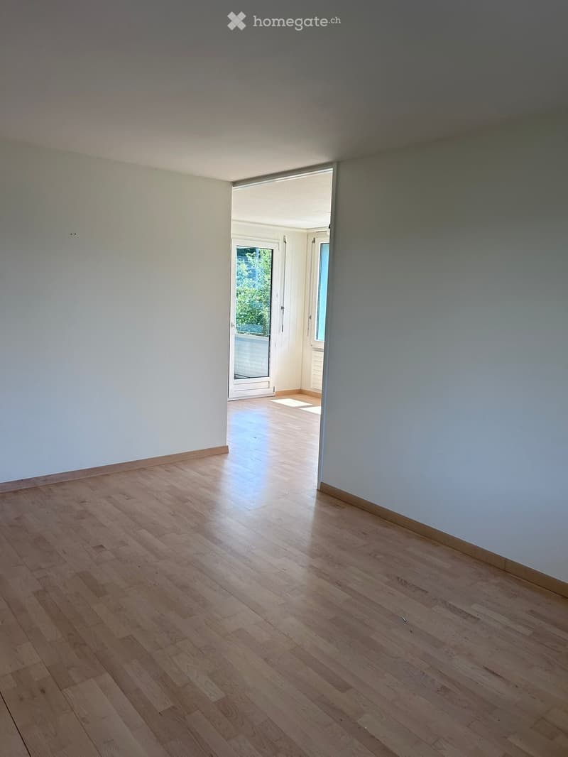 Empty room with light wooden flooring and white walls, featuring an open doorway leading to another space.