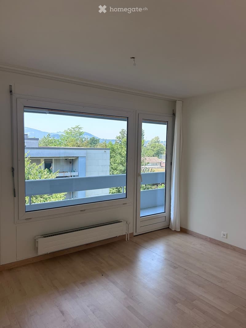 Empty room with wooden flooring, large window, and sliding door leading to a balcony.