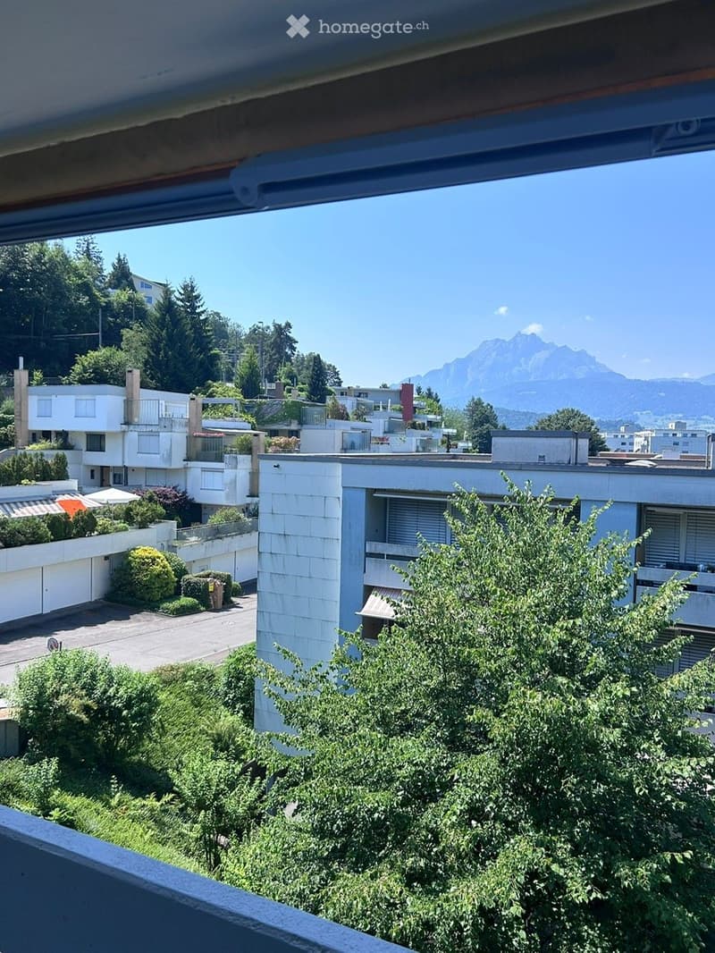 Balcony view overlooking a residential area with modern buildings, greenery, and distant mountains.