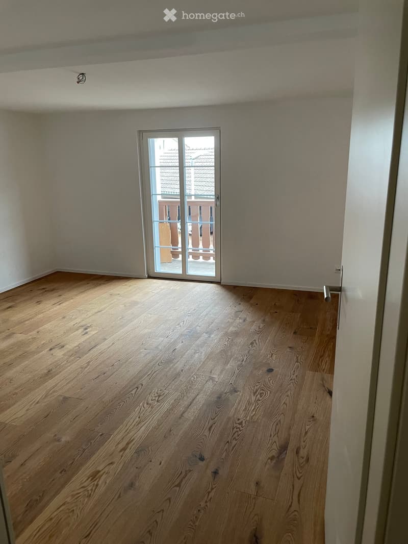 Empty room with wooden flooring and a sliding glass door leading to a balcony.