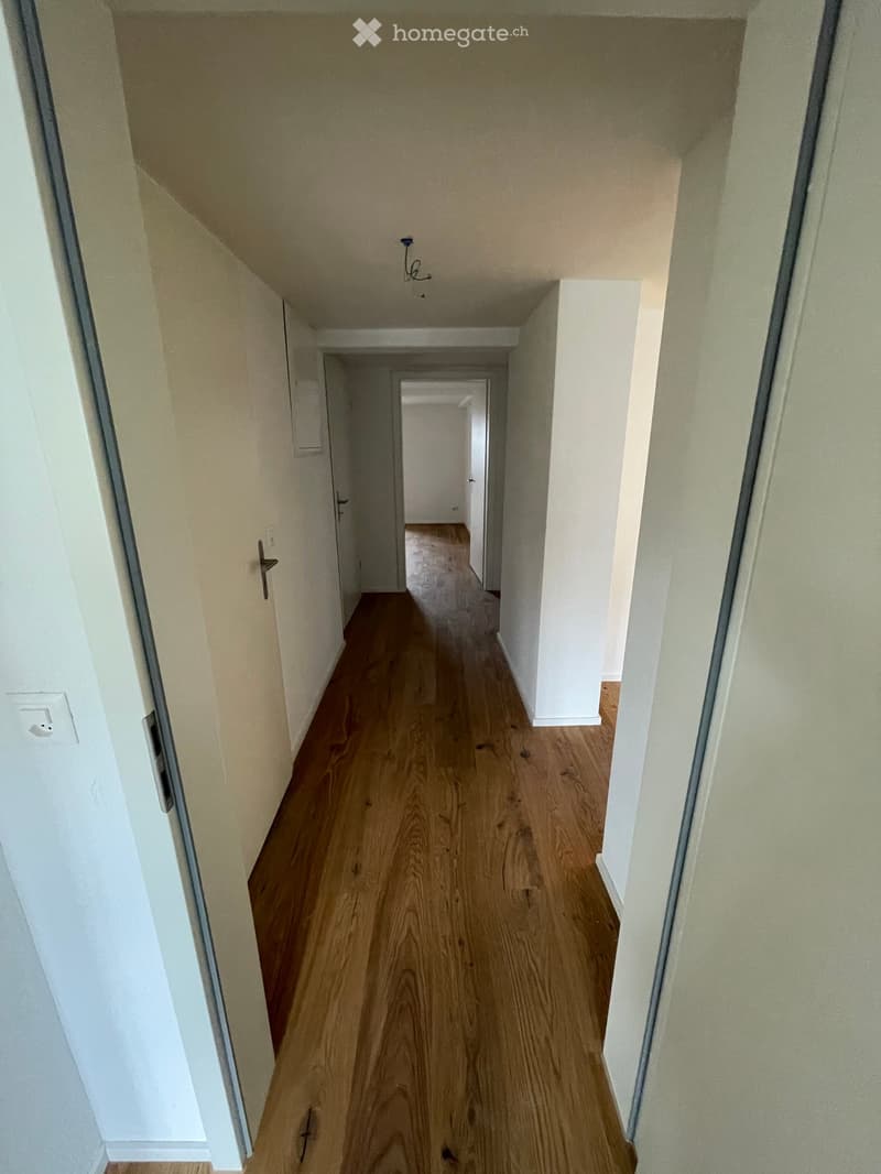 Empty hallway with wooden flooring, white walls, and multiple doors leading to other rooms.