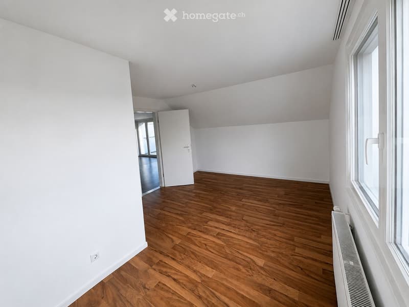 Empty room with white walls, wooden floor, large window, radiator, and a door leading to another room.