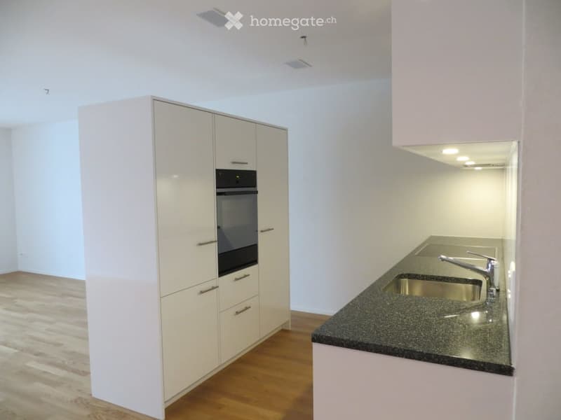 Empty kitchen with white cabinets, a built-in oven, and a granite countertop with a stainless steel sink.