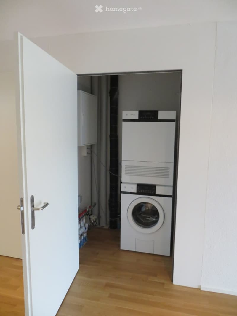 Open doorway leads to a small utility area with a washing machine and dryer, wooden flooring, and white walls.