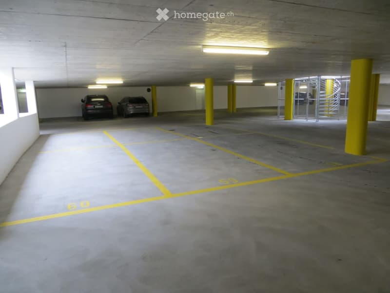 Underground parking area with concrete floors and walls, yellow parking lines, two parked cars, and yellow support pillars.
