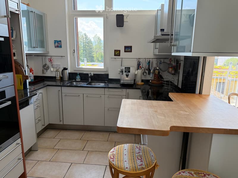 Modern kitchen with stainless steel appliances, white cabinets, a wooden island, and a small seating area with patterned stools.