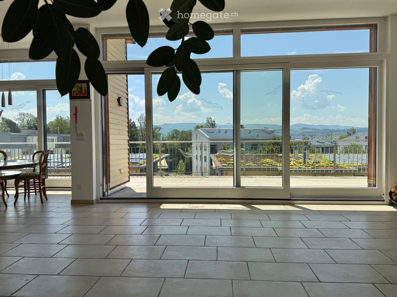 Bright room with large windows and sliding glass doors leading to a balcony, featuring a tiled floor, a small table, and chairs.