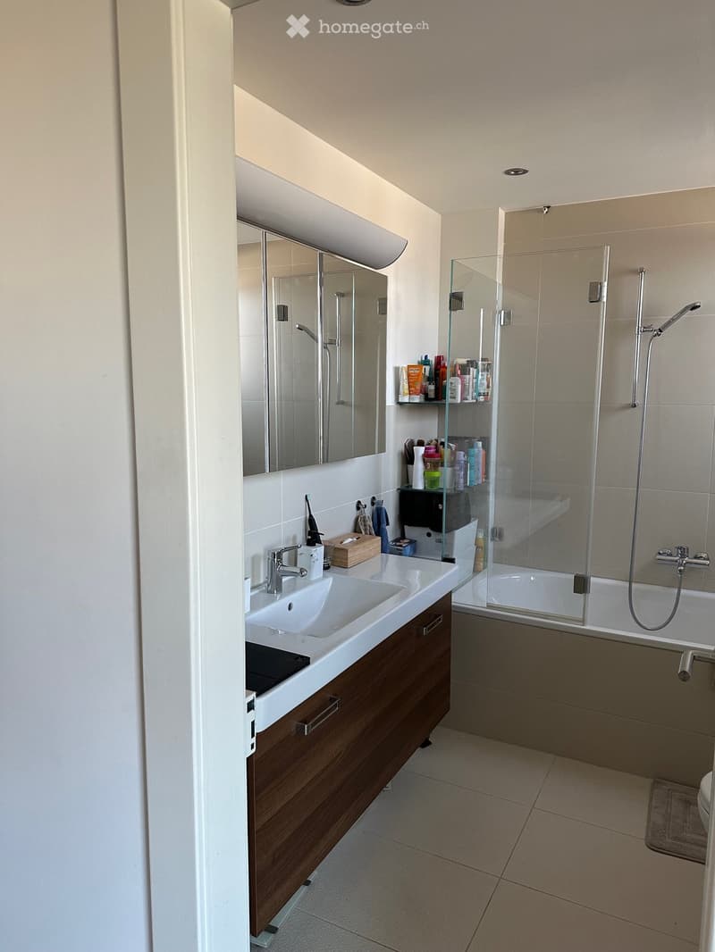 Modern bathroom with a double sink, wooden cabinet, large mirror, glass-enclosed shower, and tiled floor.