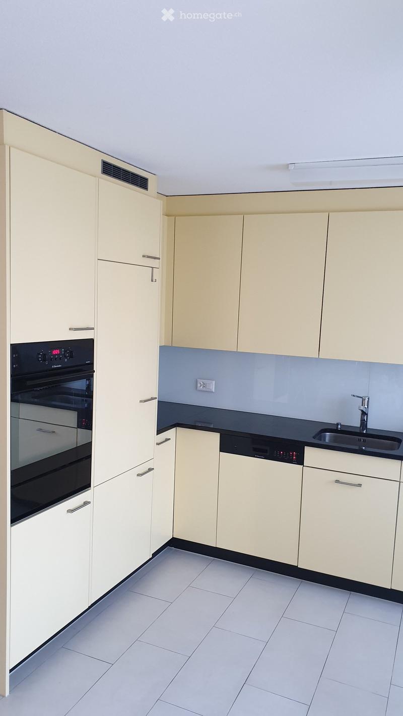 Modern kitchen with light-colored cabinets, white tiled floor, stainless steel sink, oven, and dishwasher.