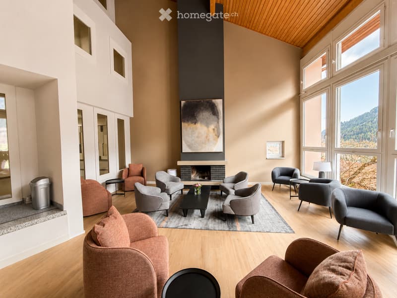 Modern living room with a fireplace, large windows offering a scenic view, multiple seating options including sofas and armchairs, coffee table, side tables, and artwork on the wall.