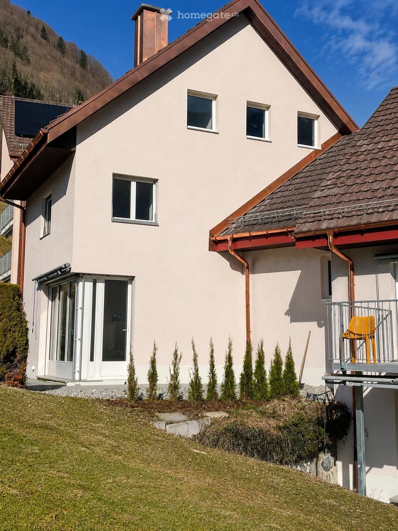 Two-story house with light beige walls, copper roof, multiple windows, and a small balcony with yellow chairs.