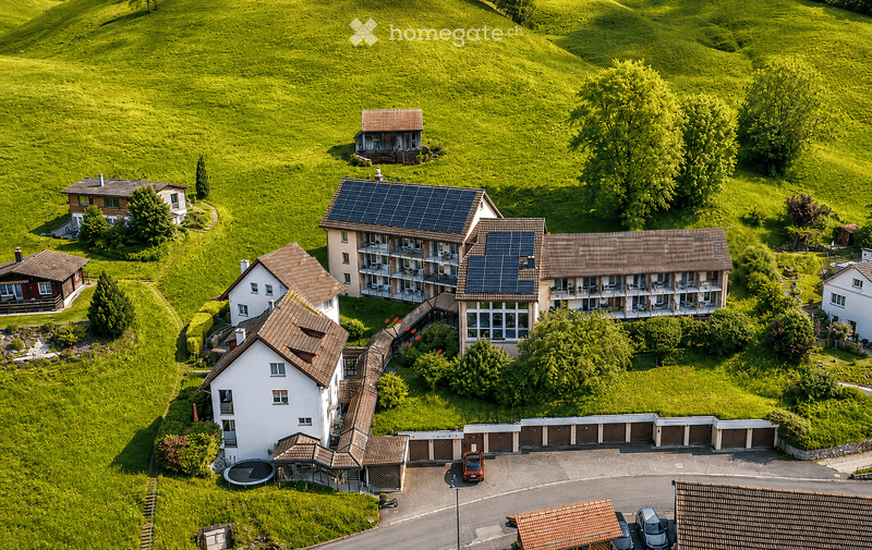 Aerial view of a residential area with multiple houses, solar panels, garages, parking area, and a swimming pool.