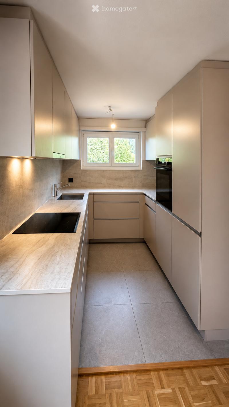 Modern kitchen with light-colored cabinets, a central island, and a window overlooking greenery. Features include an induction cooktop, sink, and built-in oven.
