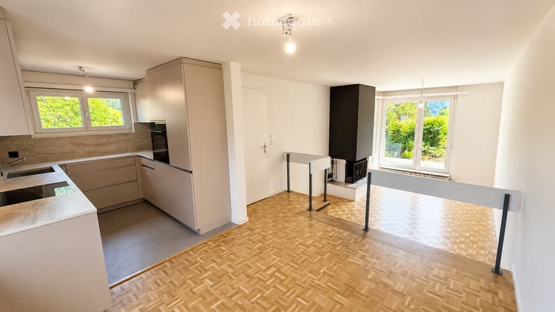 Modern kitchen with light-colored cabinets, a central island, and a wooden herringbone floor. Features include a sink, oven, refrigerator, and ample natural light from large windows.